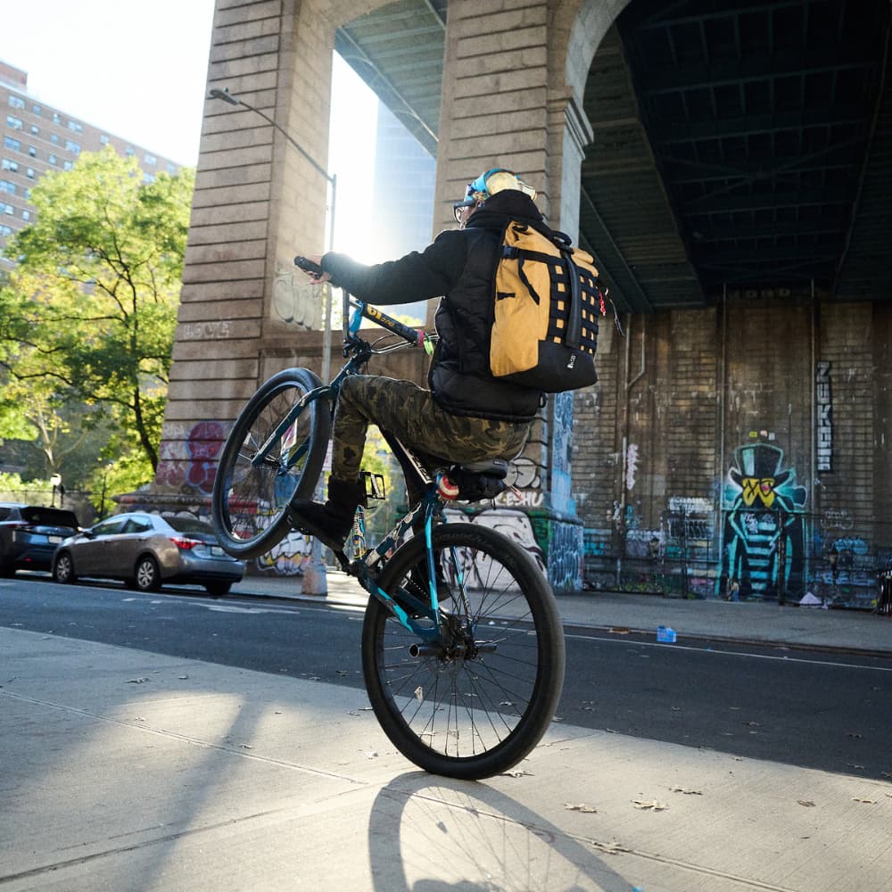 Woman riding a bike doing a wheelie wearing a barrage backpack